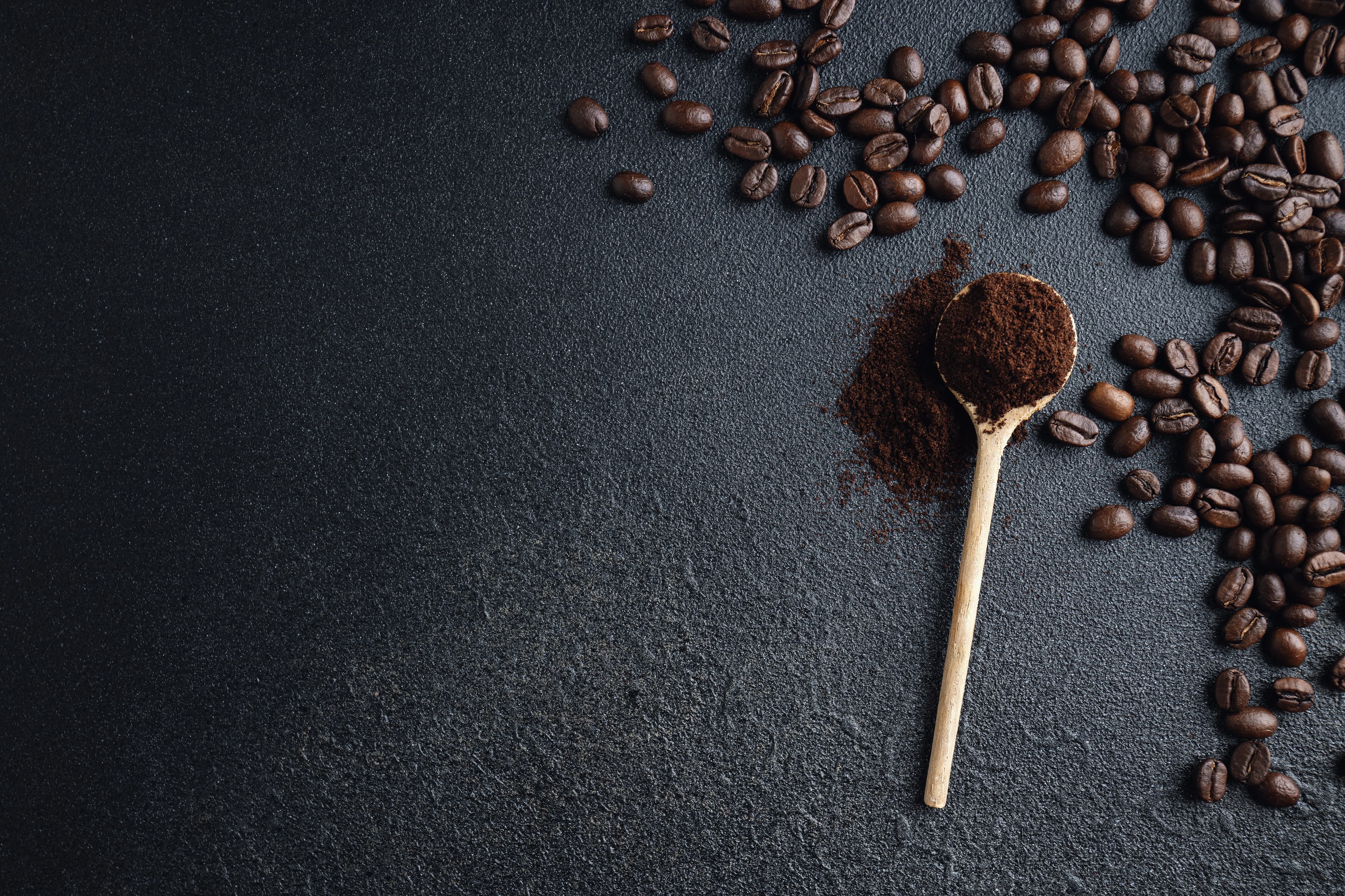 Coffee beans and ground coffee on a spoon against a dark background