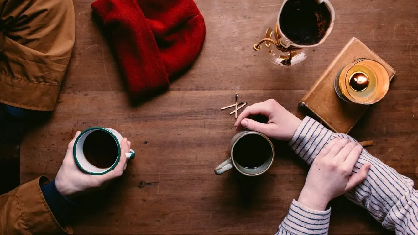 Zwei Personen mit Kaffee an einem Holztisch im Gespräch