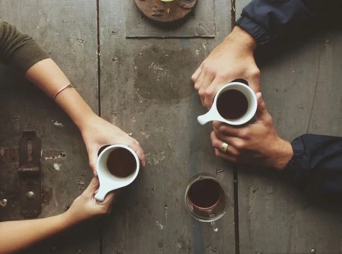 Zwei Personen mit Kaffeetassen im Gespräch an einem Holztisch
